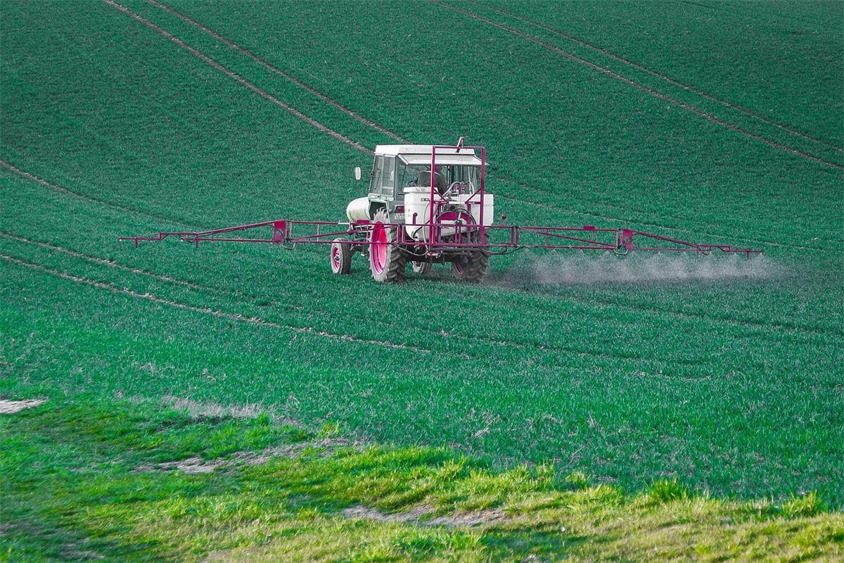 Tractor with a boom sprayer applying a crop treatment across a green field
